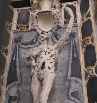 Transi of René of Chalon, a skeletal stone sculpture with one arm raised inside a church interior.