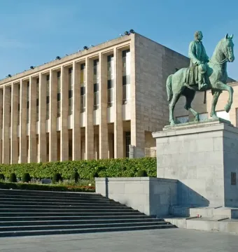 Albert I equestrian statue on a stone pedestal beside a colonnaded building in Brussels.