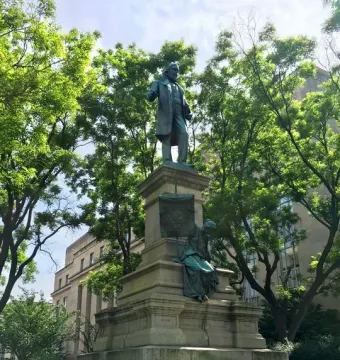 Albert Pike Memorial showing a bronze man standing atop a tall stone pedestal with a seated bronze figure below.