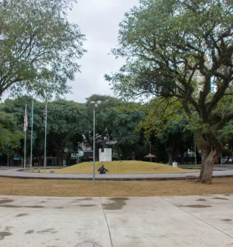 Ayrton Senna Monument on a white pedestal atop a grassy mound, with flags behind it and a person seated nearby.