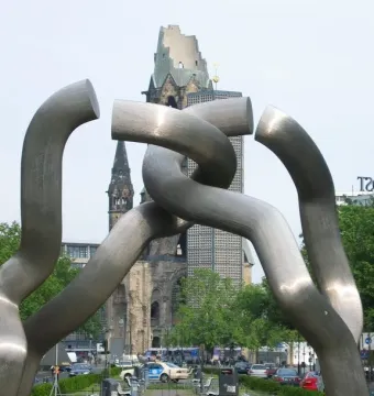 Brushed metal sculpture with interlinked tubular segments in front of the Gedachtniskirche tower.