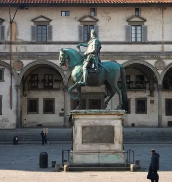 Ferdinando I de\' Medici equestrian statue on a stone pedestal in a public square with a historic building behind it.