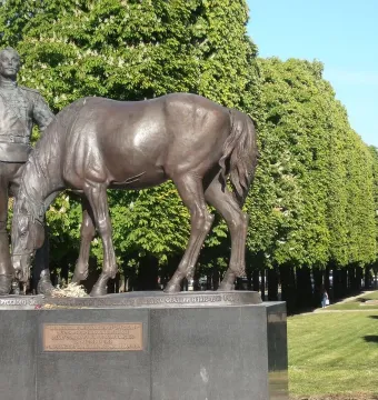 Bronze monument to the Russian Expeditionary Force showing a standing uniformed figure holding a cap beside a bowed horse on a stone base.