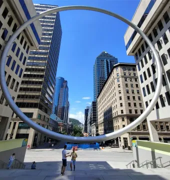 The Ring sculpture framing a city street and plaza under a bright blue sky.