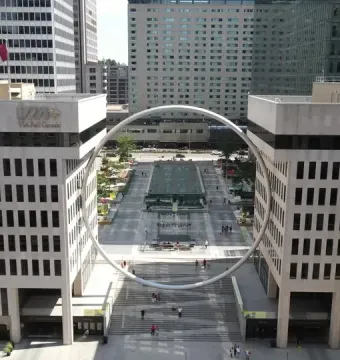 The Ring, a large circular sculpture suspended above an urban plaza between two buildings.