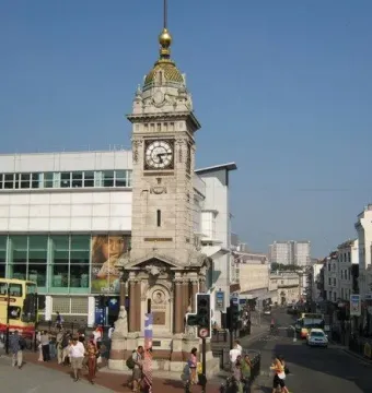 Brighton Clock Tower standing in a busy city plaza with pedestrians, a red double-decker bus, and a street beside it.