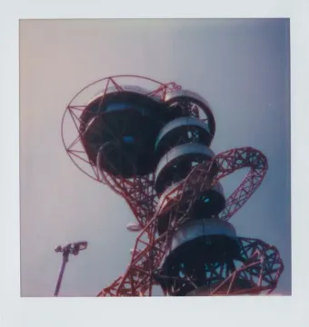Orbit Tower’s red lattice structure with dark spiral observation decks against a pale sky.