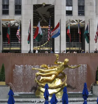 Prometheus sculpture at Rockefeller Center, a golden reclining figure above a fountain with flags overhead.