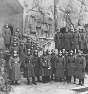 Soldiers posed on steps below the Externsteine Relief carved into the rock face.