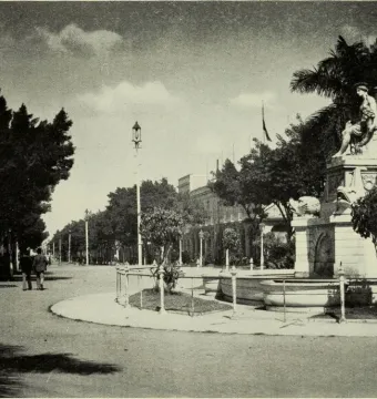 Fuente de la India, a multi-tiered stone fountain with a seated classical female statue atop a tall pedestal in a tree-lined plaza.
