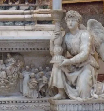 Michelangelo\'s Angel kneeling and holding an ornate candelabra beside carved marble relief.