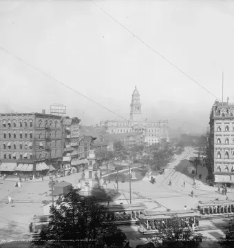 Michigan Soldiers\' and Sailors\' Monument in a busy Detroit square with streetcars, pedestrians, and horse-drawn carriages