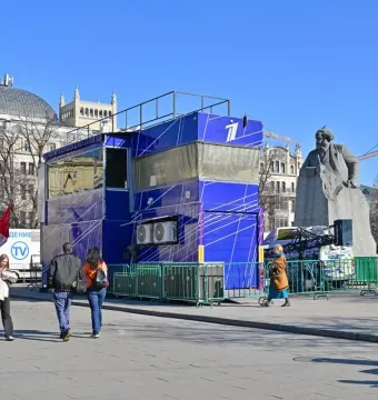 Monument to Karl Marx in a public square, partly obscured by a blue structure and green barriers.