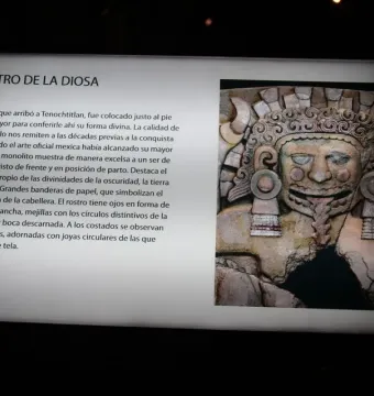 Museum display board showing the Tlaltecuhtli Monolith with Spanish text and a carved stone face with an open mouth, tongue, and elaborate headdress.