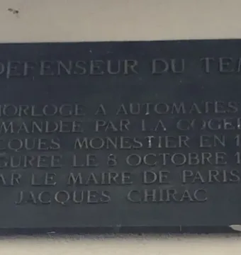 Plaque for Le Défenseur du temps with engraved French text on a dark rectangular panel.