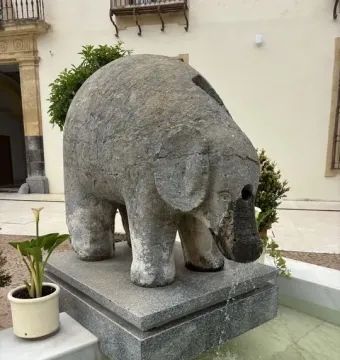 Stone elephant fountain standing on a granite base with water flowing from its trunk into a shallow basin.
