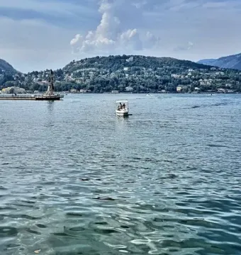 Life Electric sculpture rising from a pier on Lake Como, with mountains and lakeside towns in the distance.