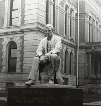 The Lincoln Monument in Wabash, Indiana, showing a seated Lincoln sculpture on a pedestal with an inscription, in front of a stone building with arched windows.