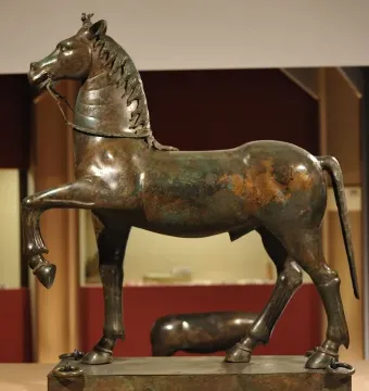 Bronze horse sculpture from the Neuvy-en-Sullias Hoard with one front leg raised, showing a green and brown patina on a rectangular base.