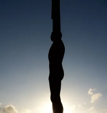 The Angel of the North silhouetted against a bright sky, with small figures near its base.