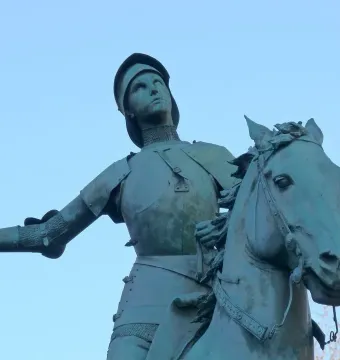 Joan of Arc statue on horseback, holding a sword upright against a blue sky