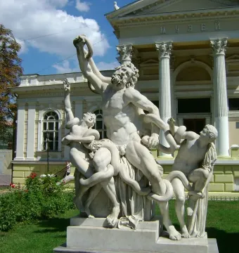 Laocoön marble sculpture group showing three figures struggling with large snakes on a lawn beside a classical building