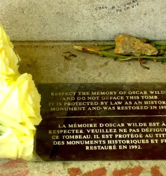 Protective plaque on Oscar Wilde\'s tomb with yellow roses beside it.