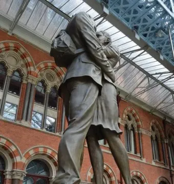 The Meeting Place bronze sculpture of a couple embracing beneath a large glass roof.
