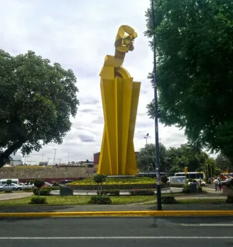 Ángel Custodio, a bright yellow abstract sculpture with tall twisting geometric forms, stands on a landscaped traffic island.