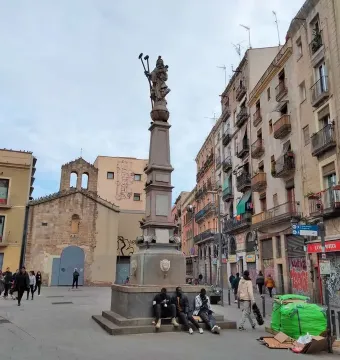 Font de Santa Eulàlia, a tall stone fountain monument in a city square with people seated around its base.