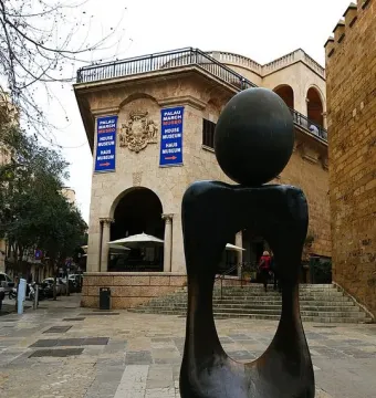 Monument a la dona by Joan Miró, a dark abstract sculpture with a sphere on a curved base in front of a historic stone building.