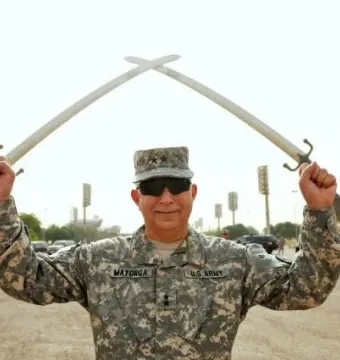 The Victory Arch with crossed swords towers in the background while a uniformed soldier stands in the foreground holding smaller swords.
