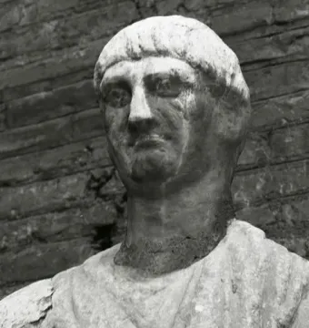 Weathered stone bust of Abbot Luigi with a serious expression, set against a dark brick background.