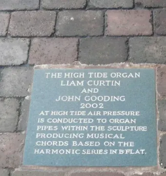 Greenish-blue High Tide Organ information plaque set into brick pavement.