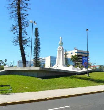 Divino Salvador del Mundo monument with a robed figure standing on a blue globe above a tiered pedestal in a park.