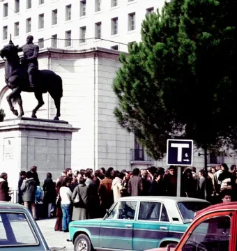 Equestrian Statue of Francisco Franco on a tall stone pedestal in an urban square with trees, cars, and a crowd nearby.