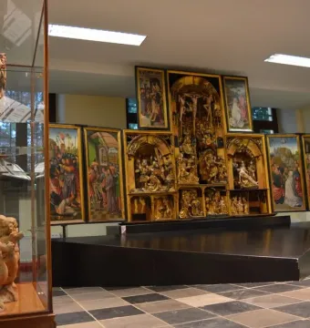The Fisenne Altarpiece with gilded sculptural reliefs and painted side panels on a dark display stand.