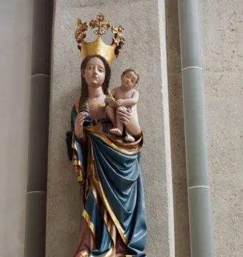 Inkpot Madonna statue of a crowned woman in blue and gold robes holding a child and an inkpot-like vessel.