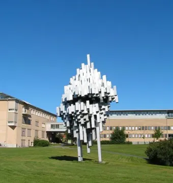 Norra skenet sculpture with white rectangular forms rising on a green lawn near campus buildings