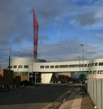 Aspire, a tall red sculpture, rises above a modern curved white building against a partly cloudy blue sky.