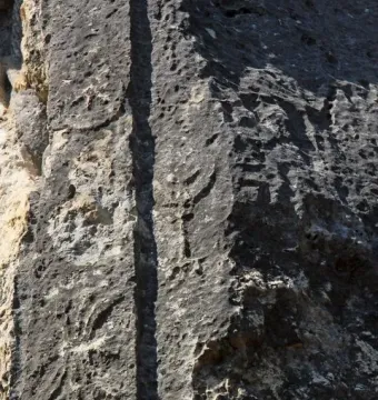 Weathered Athena relief carved into a rough stone surface with a vertical groove and faint eroded details.