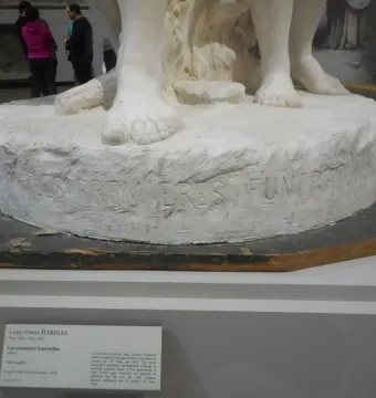 Close-up of The First Funeral sculpture showing the carved inscription and several bare feet on the plaster base.