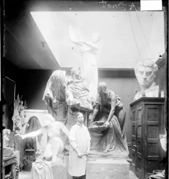 Clay or plaster models of the Fountain of the Great Lakes sculpture group stand in an artist’s studio with a man in an apron among them.