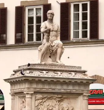 Giovanni delle Bande Nere statue on an ornate pedestal in a busy square with bicycles and pedestrians nearby.