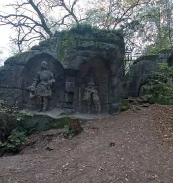 Klácelka stone reliefs in a wooded setting, with carved figures in recessed niches and iron gates in front.