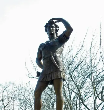 Leif Ericson bronze statue on a pedestal, with one hand raised to his brow against a bright sky.