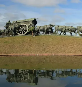 Monument to the Cart bronze sculpture showing a covered wagon, a man on horseback, and a long line of oxen beside a reflective pond.