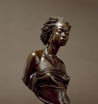 The Nubian Woman bronze bust of a woman with braided hair, hoop earrings, and a beaded necklace on a fluted pedestal.