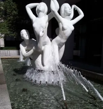 The Quest sculpture, a white marble fountain with nude figures in dynamic poses and water jets around the basin.