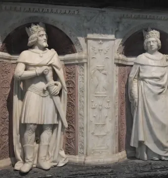 Marble statues of a crowned man holding a sword and a crowned woman in the Tomb of Francis II, set in an ornate carved niche.